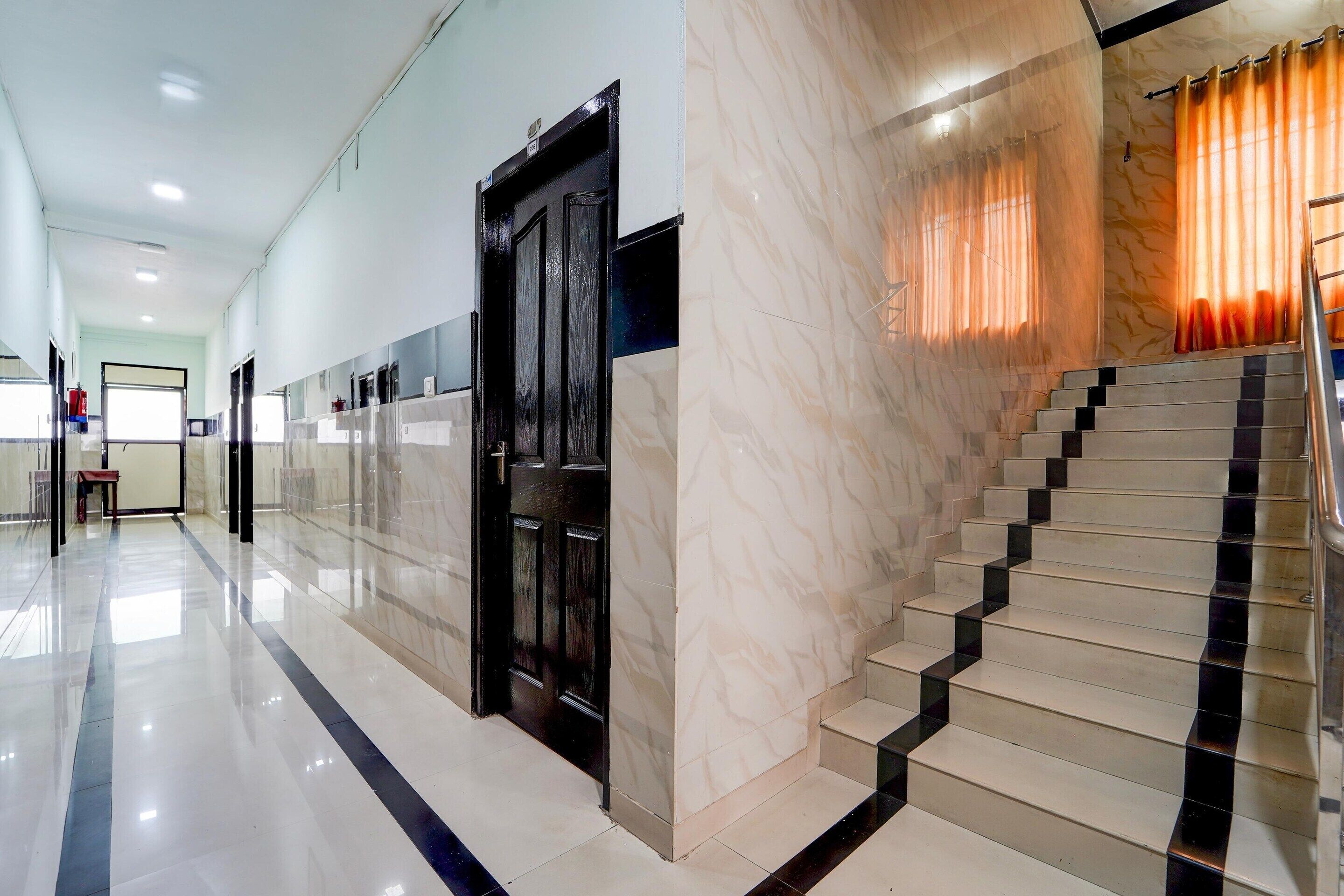 Un hall d’hôtel avec un escalier en marbre, une porte noire et une vue sur le couloir.