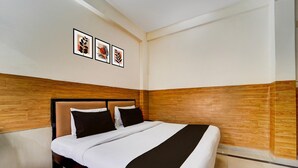 A hotel room with a bed, wooden paneling, and three framed pictures on the wall. - Deluxe Kakkanad Diamond (Kanayannur)