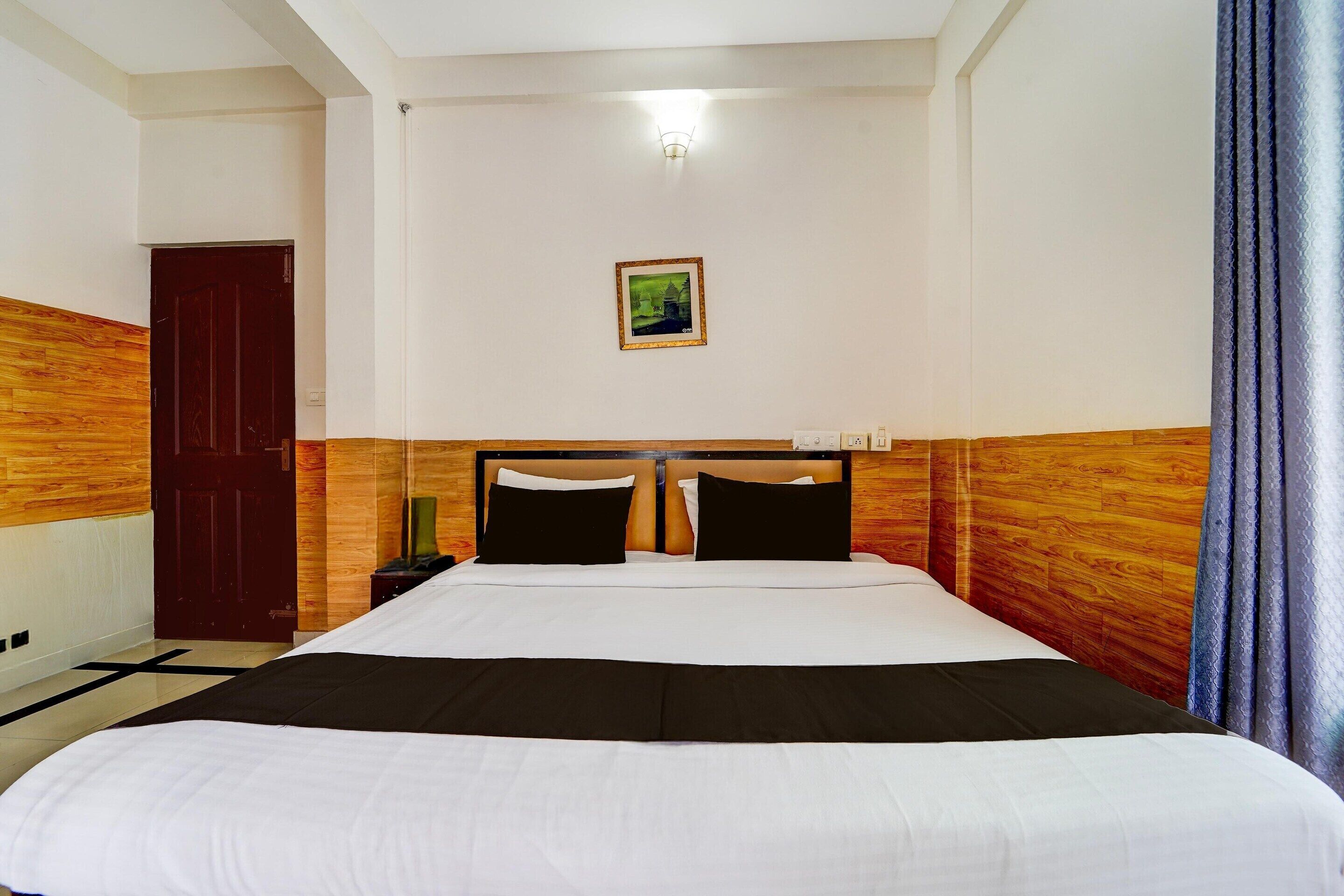 Ein Hotelzimmer mit einem großen Bett, einem hölzernen Kopfteil, einem Nachttisch, einer Lampe, einem gerahmten Bild an der Wand und einer Tür.