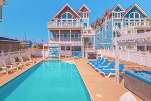 Una piscina con lettini, una zona relax coperta e un edificio con numerosi balconi.