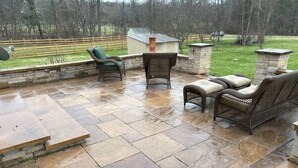 Eine Terrasse mit Steinfliesen, Korbmöbeln und einem Kamin aus Stein.