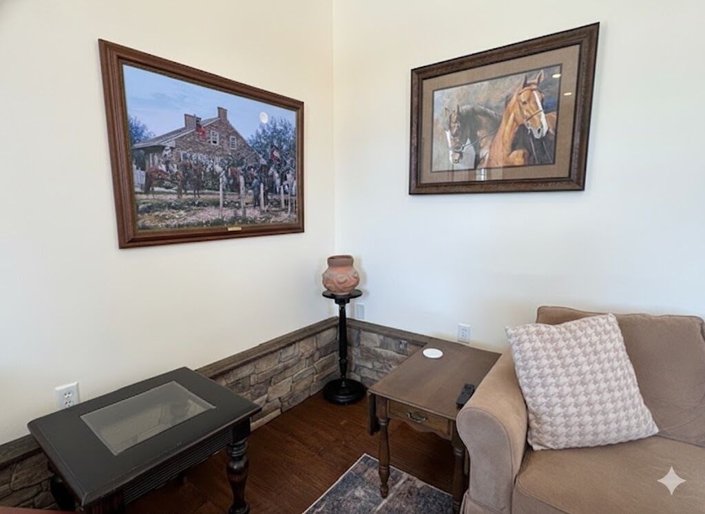 A living room with a glass-top table, a sofa, a small table, and two framed pictures on the wall.