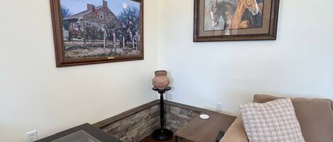 A living room with a glass-top table, a sofa, a small table, and two framed pictures on the wall.