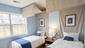 Ein Schlafzimmer mit zwei Betten, einem Fenster, einem Nachttisch und einer Lampe.