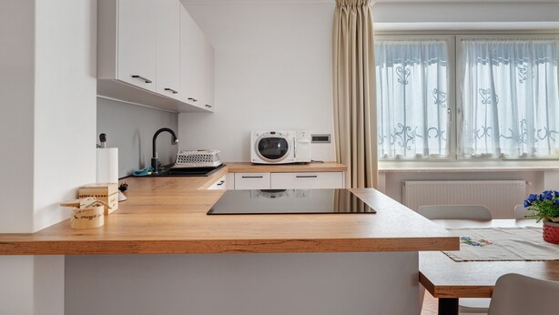 Een moderne keuken met witte kasten, een houten aanrecht, een magnetron en een raam met gordijnen.
