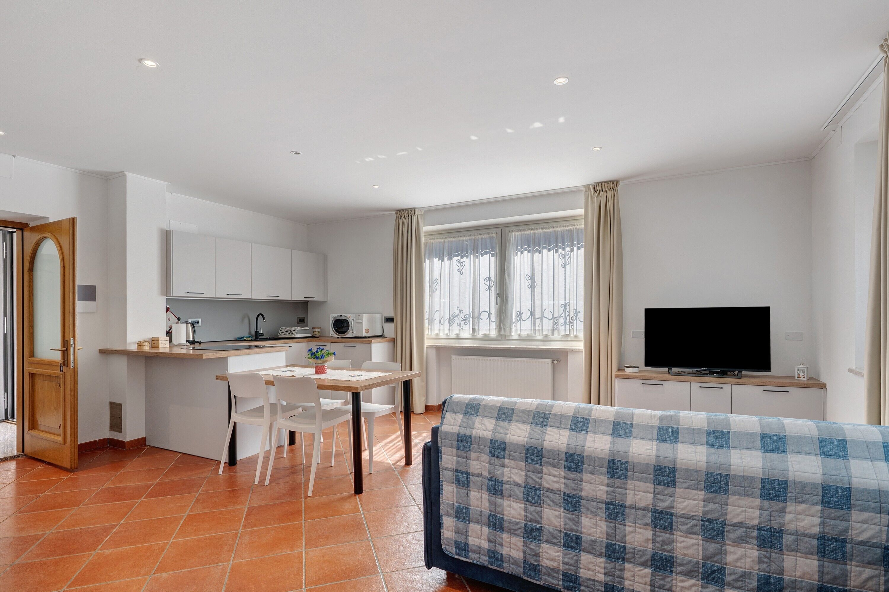 A compact living space with a kitchenette, a dining area, a television, and a bed with a checkered blanket.