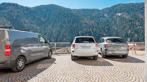 Een parkeerplaats met twee voertuigen, een bestelwagen en een personenauto, en een bergachtig landschap op de achtergrond.