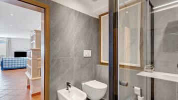 A modern bathroom with a bidet, toilet, and glass shower enclosure.