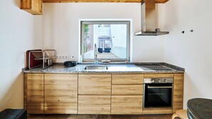 A modern kitchen with wooden cabinets, a stainless steel sink, a built-in oven, and a window overlooking a street. - 2-bedroom villa in beautiful Faro with cool AC breeze (Faro)