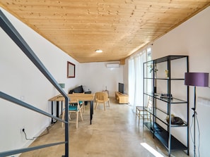 A modern interior with a wooden ceiling, a dining area with a table and chairs, a black shelving unit, and a television. - 2-bedroom villa in beautiful Faro with cool AC breeze (Faro)