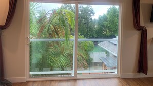 Quarto com uma grande porta de correr de vidro que dá para um quintal com vegetação e cerca branca.