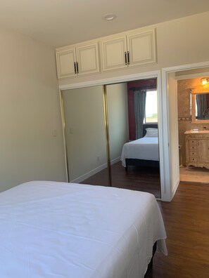 Une chambre à coucher comprenant un lit, une armoire, un miroir et une salle de bain avec un lavabo et un meuble-lavabo.