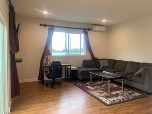 Un salon avec un canapé, un bureau, une chaise, une lampe et une fenêtre avec des rideaux.