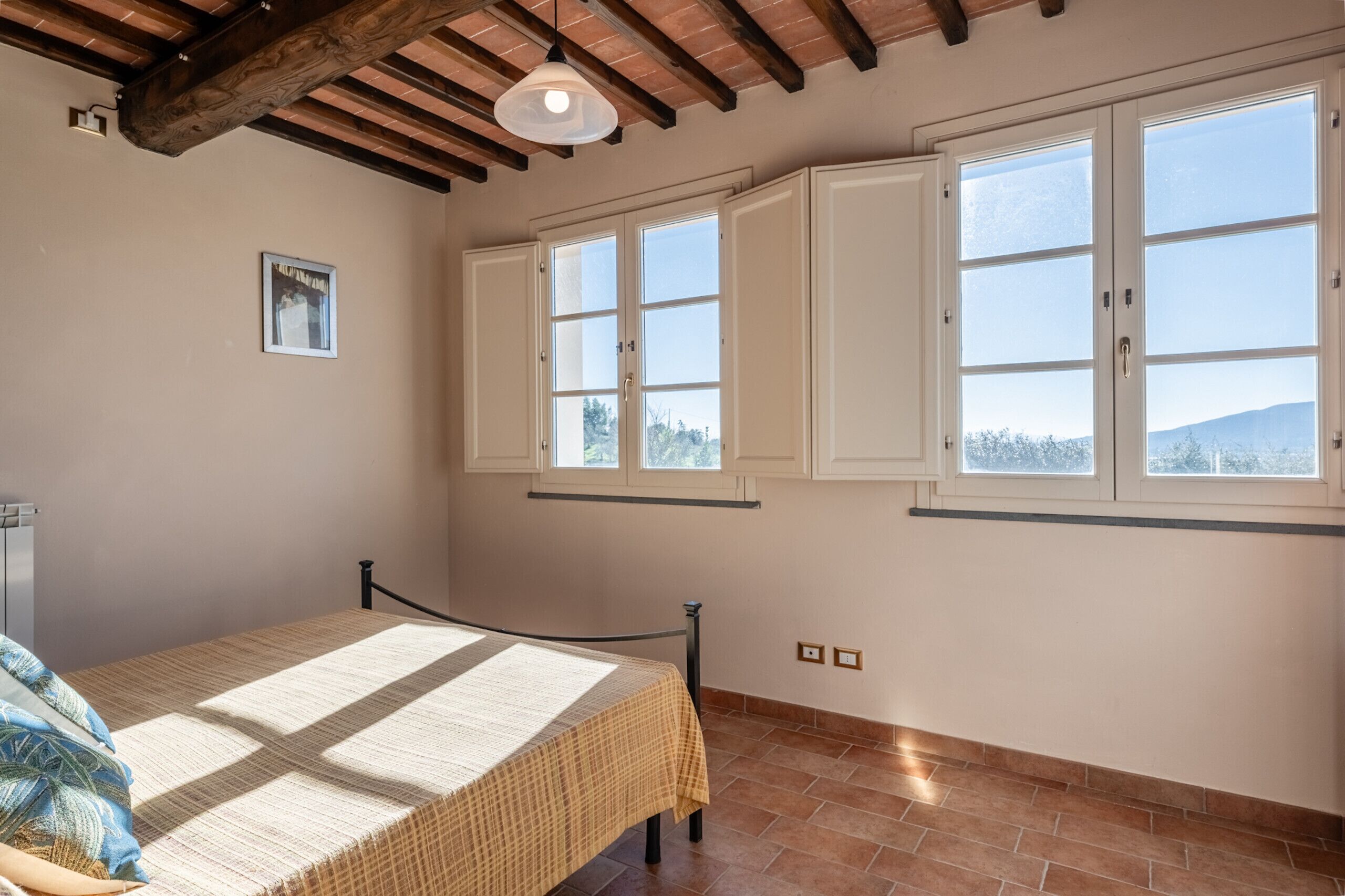 Une chambre à coucher avec un lit, une fenêtre et un plafond avec des poutres apparentes.