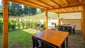 A covered patio area with a wooden table and chairs, surrounded by a fence and greenery. - Il Girasole Apartment with Swimming Pool (Capannori)