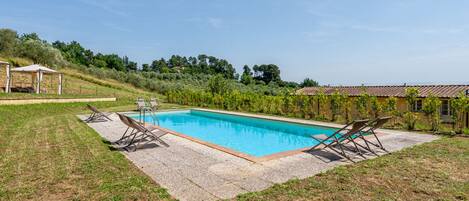 Una piscina rectangular con solárium empinado, rodeada de césped y algunas sillas de descanso.