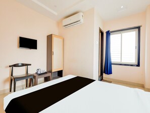 A hotel room with a bed, a television, a wardrobe, a desk with a chair, and a window with curtains.