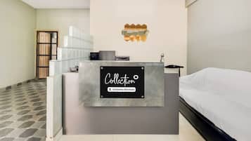 A hotel room with a reception desk, a bed, a ceiling fan, and a geometric wall decoration.