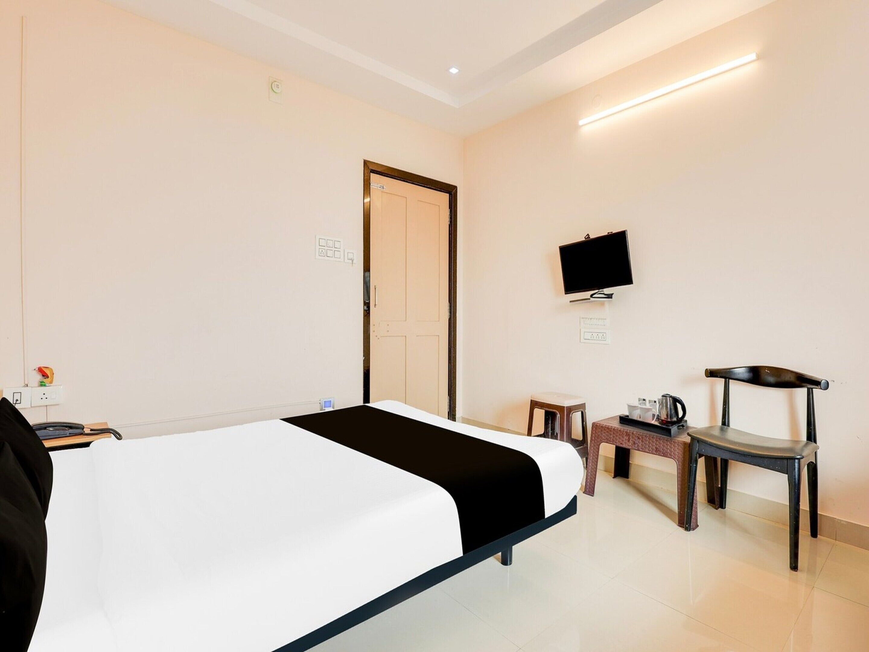 A hotel room with a bed, a TV, a chair, and a small table with a coffee maker.