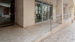 Une entrée d’immeuble avec un sol carrelé, une porte en verre et une rambarde en métal.