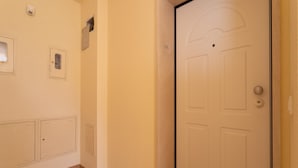 Un couloir avec une porte blanche, une petite fenêtre et un interrupteur fixé au mur.