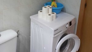Un lavadero pequeño con lavadora, inodoro y lavamanos azul con un objeto amarillo.