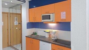 Una cocina compacta con microondas, lavamanos y un refrigerador pequeño.