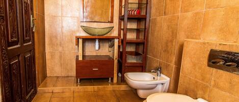 A bathroom with a wooden door, a vessel sink, a cabinet, a bidet, and a toilet.