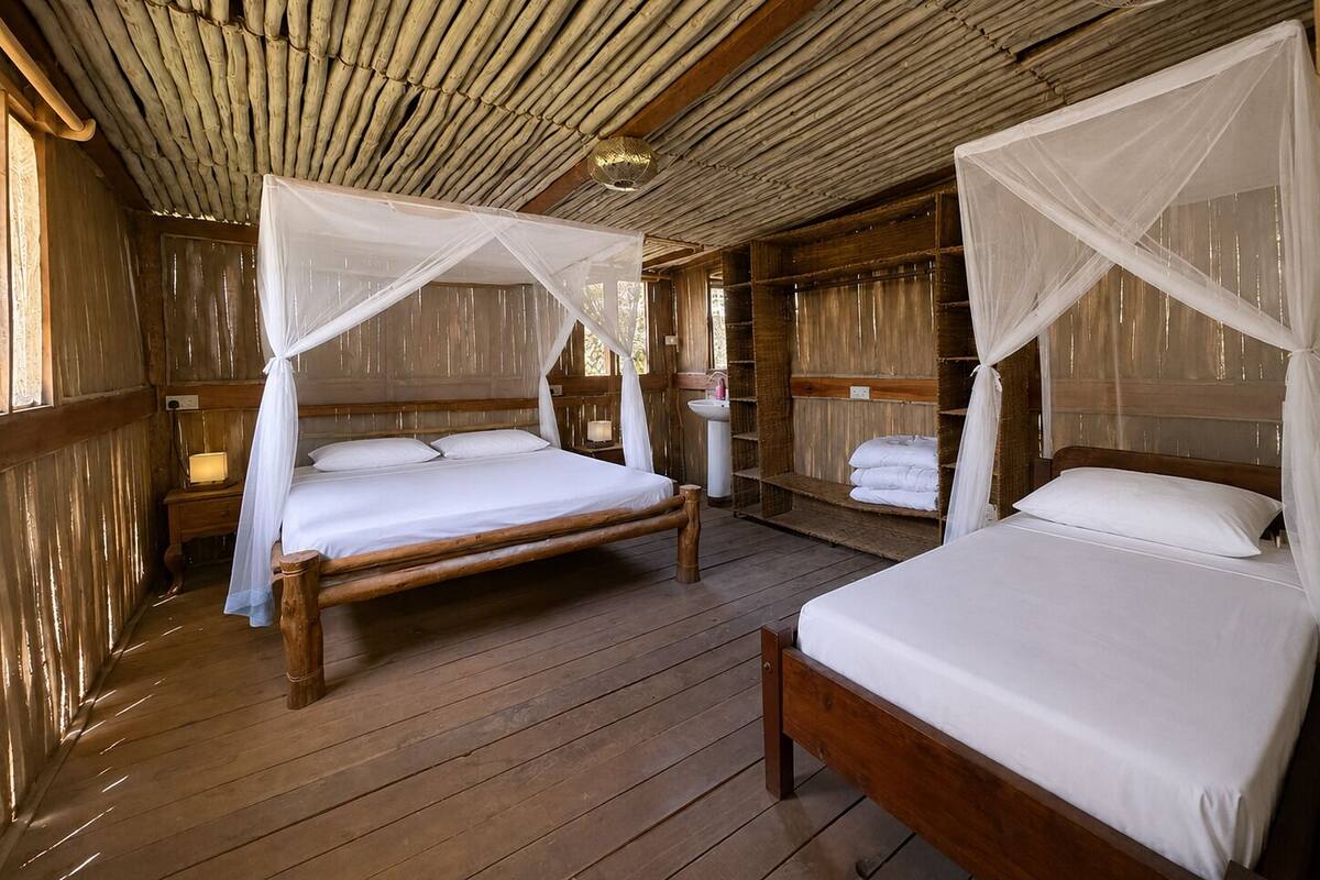 Two wooden beds with white bedding and mosquito nets, wooden floors, and a rustic wooden ceiling.