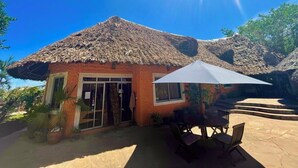 Ein Gebäude mit einem Strohdach, einer Terrasse mit Tisch und Stühlen sowie einem großen Sonnenschirm.