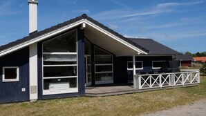 Ein modernes Haus mit einem großen Fenster, einem Schornstein und einer Terrasse mit Gartenmöbeln.