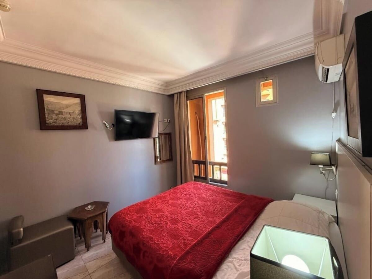 Une chambre d’hôtel équipée d’un lit, d’un bureau, d’une chaise, d’une télévision et d’une fenêtre avec des rideaux.