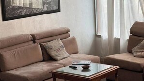 Ein Wohnzimmer mit einem beigen Sofa, einem Glastisch und einem gerahmten Bild an der Wand.