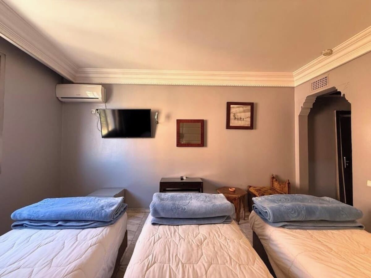 Ein Hotelzimmer mit drei Betten, einem Flachbildfernseher, einem kleinen Tisch und einer Tür.