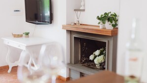 Une pièce avec une cheminée, un téléviseur fixé au mur, un bureau blanc et une table à manger avec des chaises.