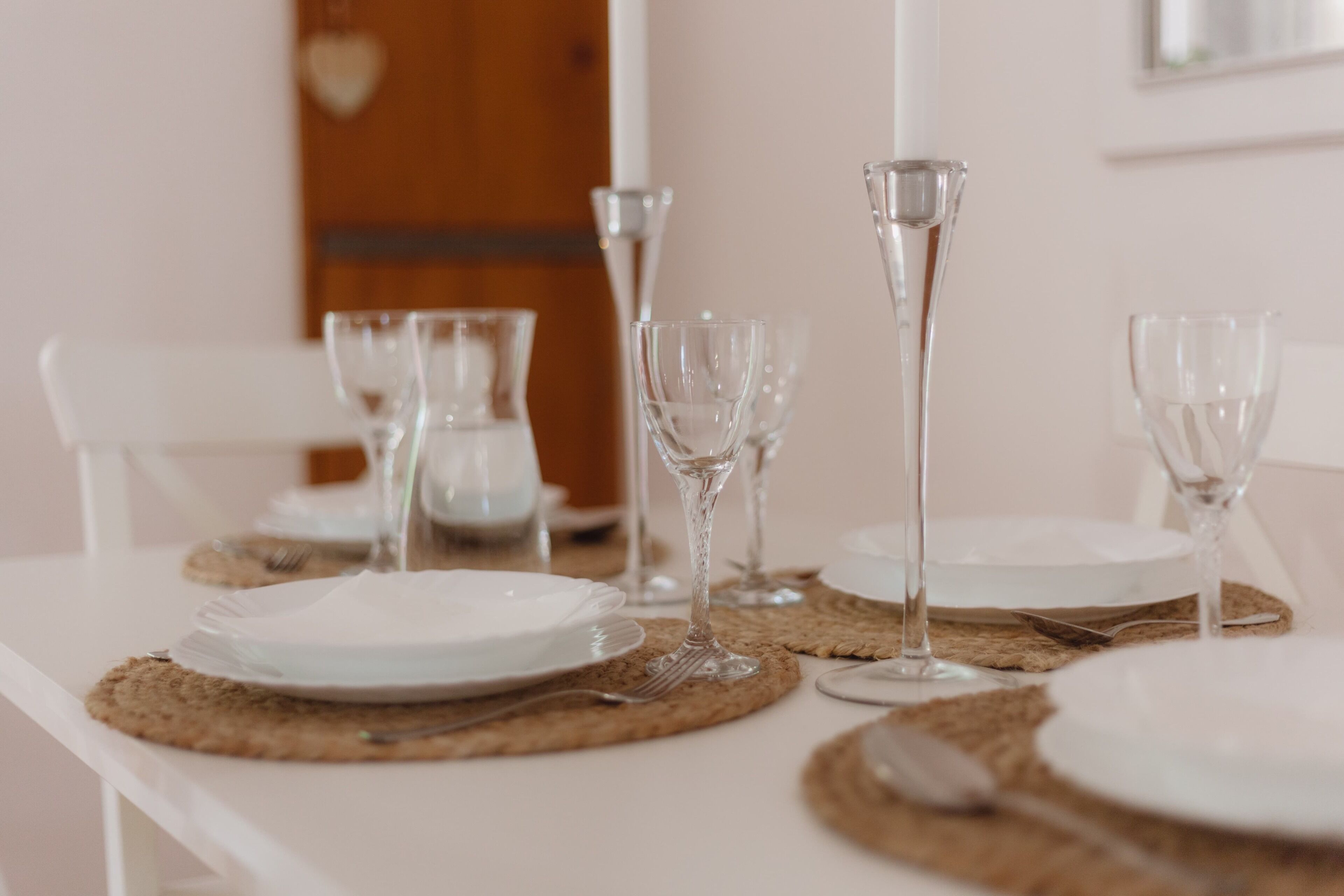 Een gedekte tafel met borden, bestek en wijnglazen, met een witte tafeldoek en geweven placemats.