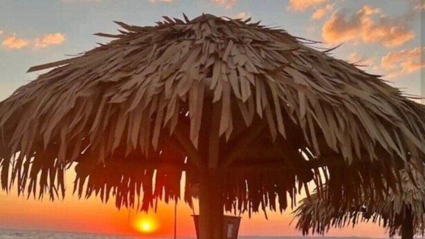 Une plage avec un parasol en chaume, des chaises longues et une vue sur le coucher de soleil.