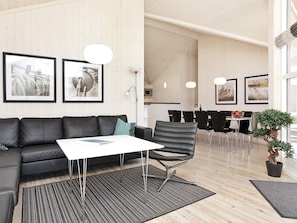 A modern living room with a sofa, a coffee table, and a dining area with chairs and a table. - 4 Star Holiday Home in Grossenbrode (Grossenbrode)