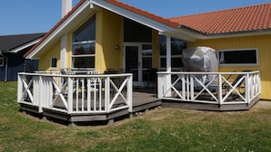 A yellow building with a red-tiled roof, a covered patio with white railings, and a chimney. - 4 Star Holiday Home in Grossenbrode (Grossenbrode)