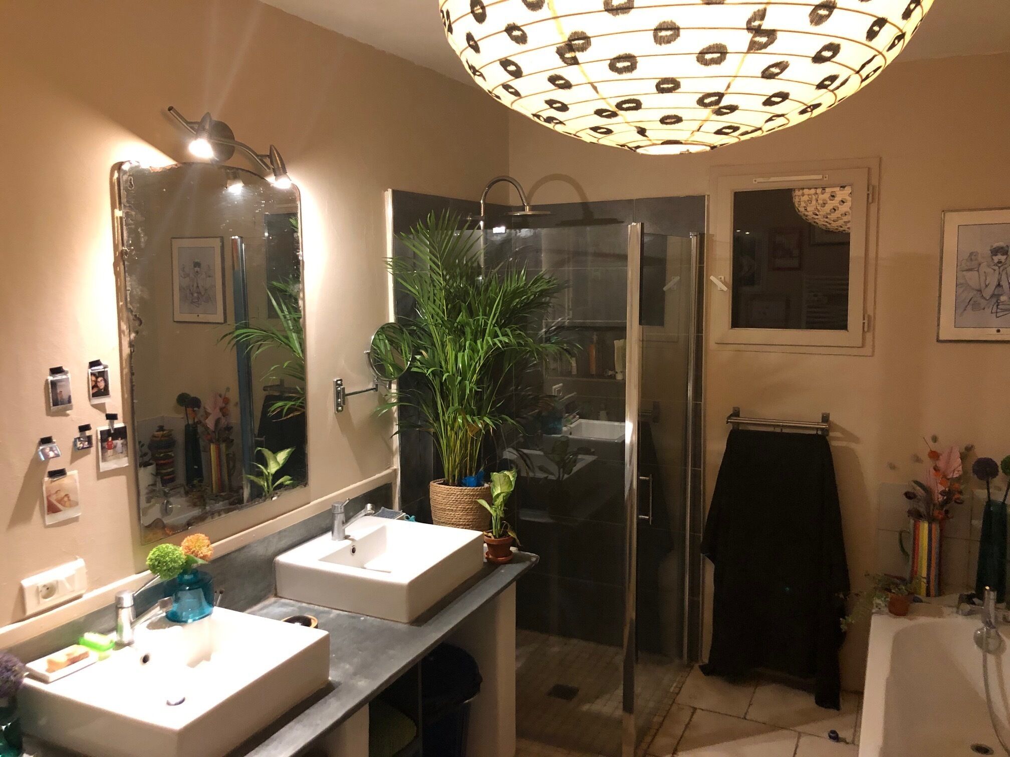Une salle de bain avec deux lavabos, une douche, un grand miroir et un luminaire au plafond.