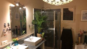 Une salle de bain avec deux lavabos, une douche, un grand miroir et un luminaire au plafond.