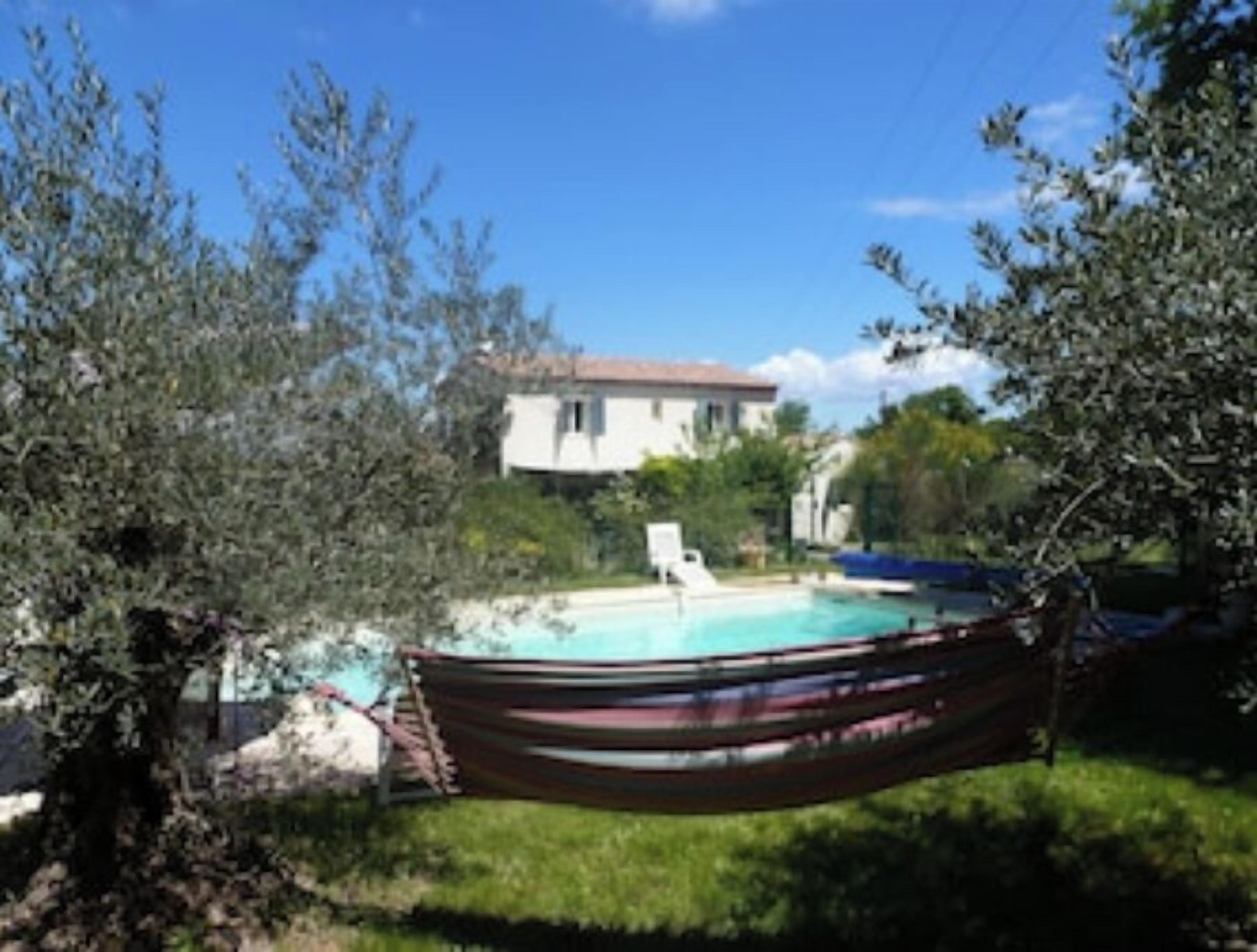 A hammock over a swimming pool with a house in the background.