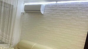 En beige sofa i et rum med en hvid murstensvæg og en aircondition installeret over den.