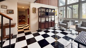 Una habitación amplia con piso a cuadros, un armario de madera empotrado, una zona de estar con sofás y ventanas grandes que ofrecen vistas al exterior.