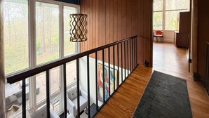 Un interior de madera con balcón, ventanas amplias y una escalera.