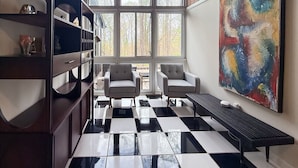 Una habitación con piso a cuadros, dos sillones, una estantería y un cuadro abstracto grande.