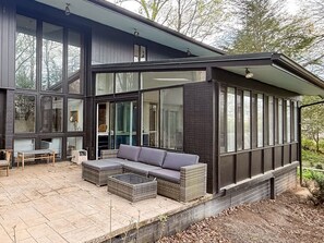 Una casa moderna con un'ampia vetrata, un patio con mobili e fondamenta in mattoni.