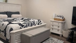 Une chambre à coucher comprenant un lit, un ventilateur de plafond, une commode, un téléviseur et une fenêtre.