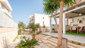 A courtyard with steps leading to a covered area, potted plants, and a palm tree.