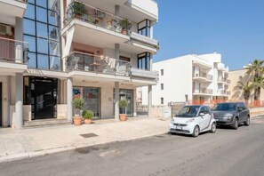A multi-story building with balconies, potted plants, and parked cars. - CarmenLeo-Central Accommodation with Patio (Polignano a Mare)